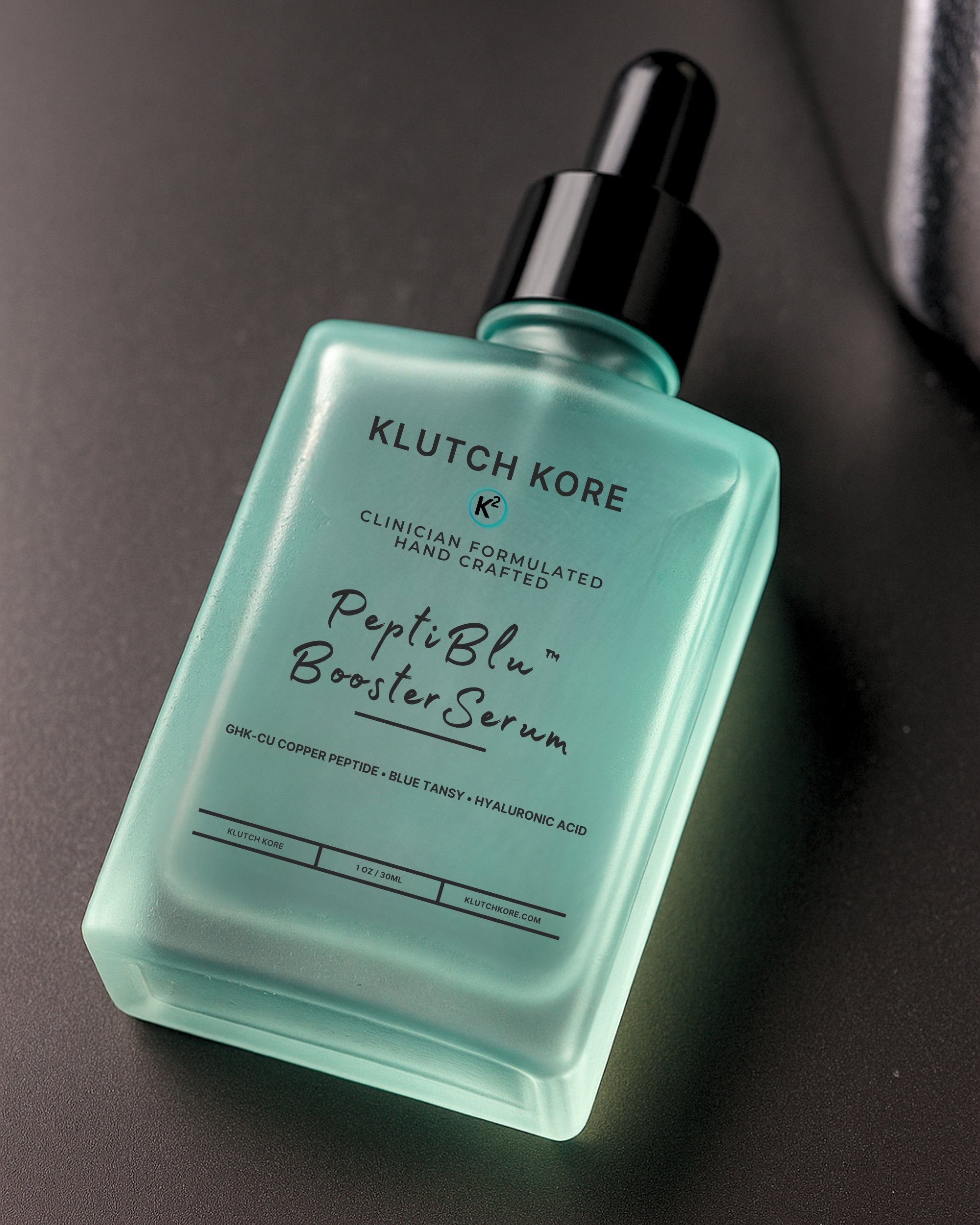 KlutchKORE PeptiBlu Booster Serum bottle angled on a dark surface